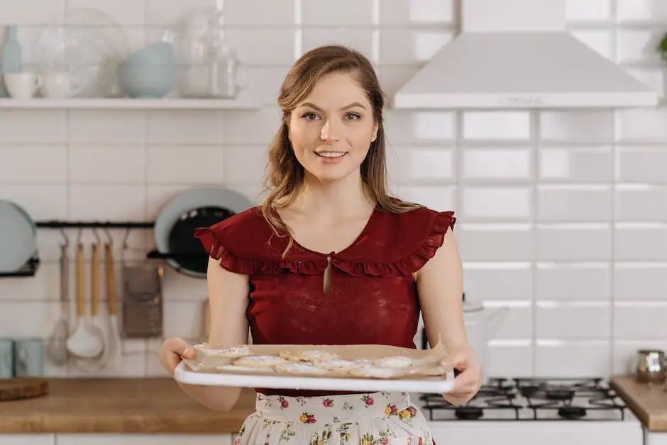 A photo of a woman in a kitchen smiling and holding a baking sheet with freshly baked cookies on it.